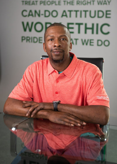 Seated Vulcraft teammate with arms folded, wearing a bright orange polo shirt.