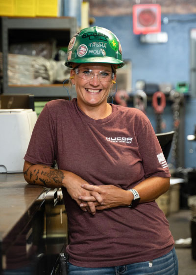 Closeup image of smiling female Nucor Vulcraft teammate wearing a reddish t-shirt and green safety helmet.